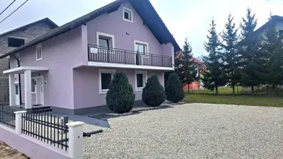 a pink house with a balcony and a driveway at Apartmani Biser Kupresa 5 in Kupres