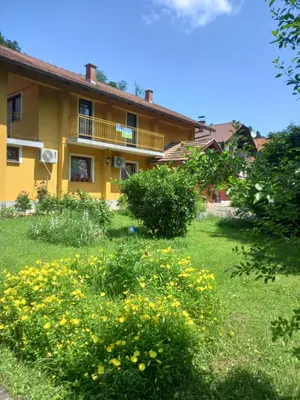 a yellow house with yellow flowers in the yard at Apartman Dujaković in Banja Vrućica